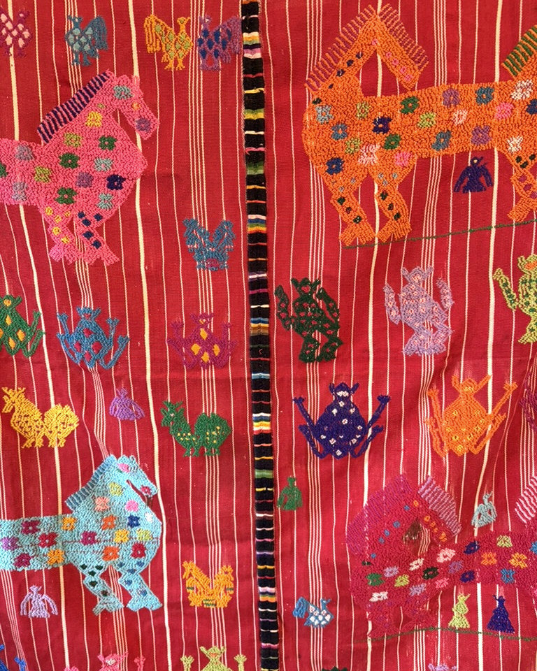 Detail of a vintage Guatemalan handwoven textile, hand-brocaded horses and frogs on a deep red ground